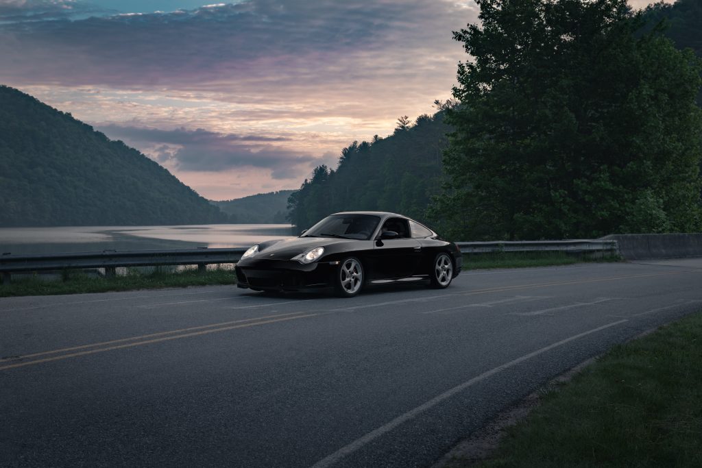 A black Porsche coupe on a bridge passing a river during evening time